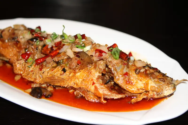 Ein ganzer gebratener Fisch in roter Soße mit Frühlingszwiebeln